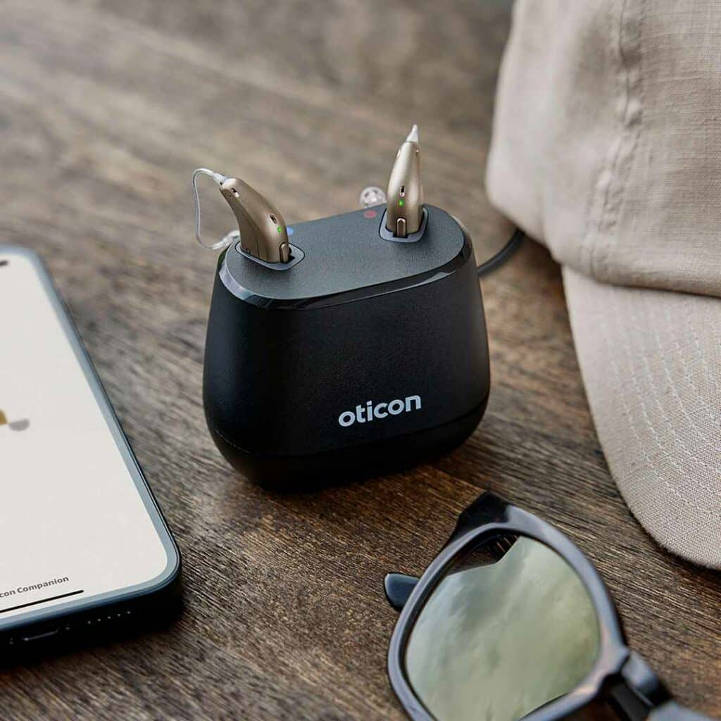 Oticon Intent Hearing Aids Charging next to baseball cap and sunglasses.